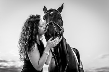 Beautiful brunette girl kissing her horse. Selective focus on horse's nose.