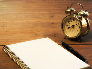 Blank notebook with vintage alarm clock and black pen on wood table