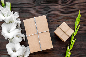Fototapeta premium Gift box wrapped in craft paper near flower gladiolus on wooden background top view copyspace