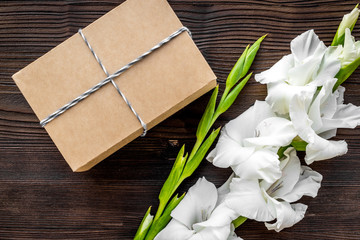 To wrap a gift. Box in kraft paper near flower gladiolus on dark wooden table top view