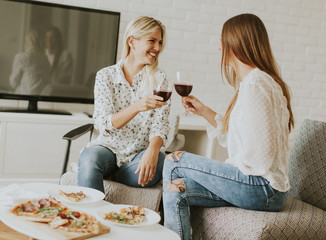 Pretty young females eating pizza and drink red wine