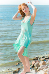 Beautiful girl in light blue bright clothes, pure makeup, relax mood, at warm day at shore. Tender stylish photography near sea. Beauty idea. Stunning young redhead woman in tunic with gold cross