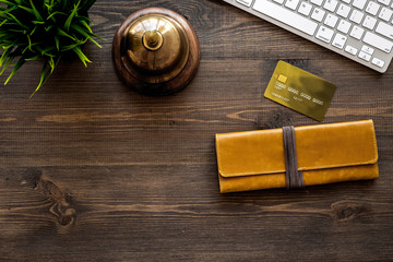 Book hotel online. Bank card and purse near service bell and keyboard on dark wooden table background top view copyspace