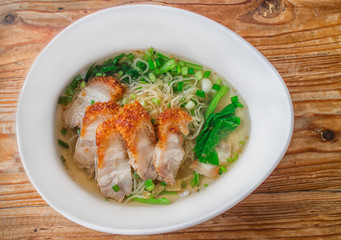 Delicious Thai egg noodles topped with crispy roasted pork on wooden background
