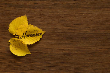 Yellow leaves with the inscription NOVEMBER on the brown wooden background.