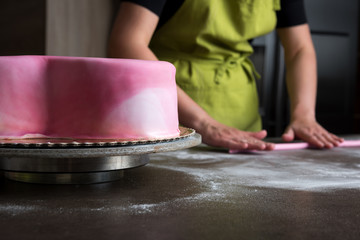 Obraz na płótnie Canvas Unrecognisable woman preparing pink fondant for cake decorating, focus on the cake
