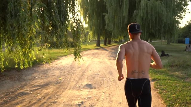 Young male runner runs down the road and listens to music in the park at sunset, slow motion