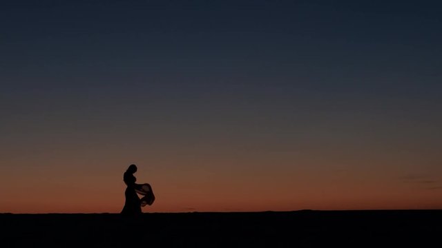 Girl is dancing belly dancing against the beautiful sunset on the beach. Silhouettes