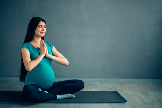 Pre-natal exercises. Beautiful pregnant woman exercising while sitting in lotus position