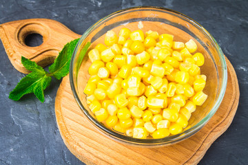 Canned corn in a glass plate on a gray concrete background.
