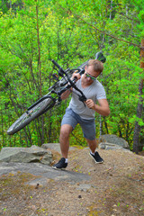 A bicyclist in glasses rises with a mountain bike across the rough terrain. Taking sports in nature. Healthy way of life
