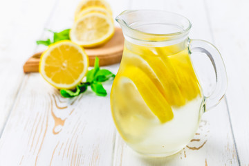 A pitcher with a cold lemonade on a white wooden background surrounded by lemons.