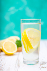 A glass jug with a cold lemonade on a white wooden background surrounded by lemons.