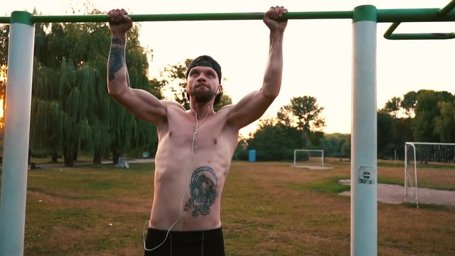 young bearded man pulls himself up on a bar in the park, slow motion