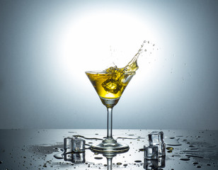 view of MARTINI GLASS getting splash by ice cube with yellow water on sloppy reflection floor