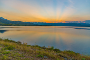 Naklejka na ściany i meble Dramatic view and magic sunbeam at sunset, mountain background. Tranquil panorama landscape of Yang Choom Reservoir, Kui Buri, Prachuap Khirikhan, Thailand.