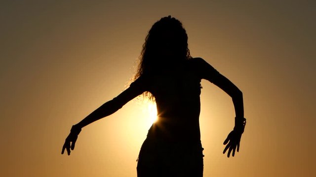Girl is dancing belly dancing against the beautiful sunset on the beach. Silhouettes