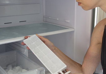 Woman hands taking ice cubes from fridge close up