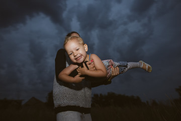 Cute baby girl playing with her mother outdoor. Flying against dark sky.