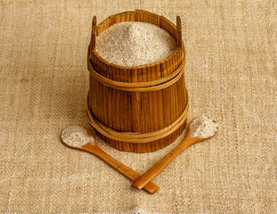 Buckwheat flour in wooden canister with two wooden spoons on sackcloth