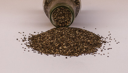 Chia seeds spilling of glass jar on white background
