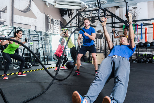 Männer und Frauen beim Crossfit Training im Fitnessstudio treiben Sport an Ringen und Seil