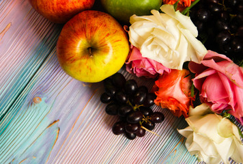 Colorful wooden background with roses, grapes and apples