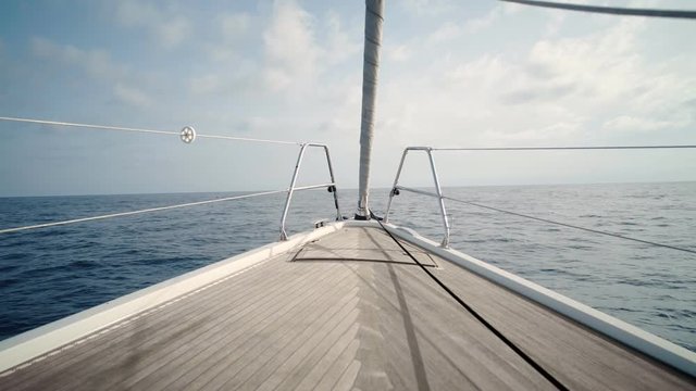 Front view on luxury sailing yacht boat nose with wooden parquet floor, swaying in open sea at sunny day. Relaxing and peaceful background holiday shot