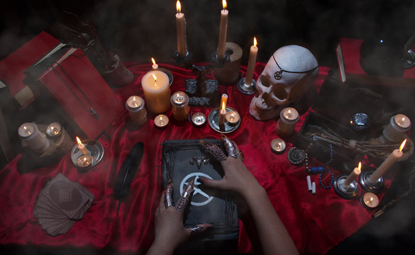 Witchcraft composition with witch's hands, satanic magic books, skull, candles, tarot cards, crystal and amulets. Halloween and occult concept, black magic ritual. 
