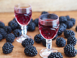 Blackberry liqueur in crystal glasses and blackberries on wooden background