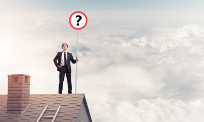 Businessman on brick house roof showing banner with question mar