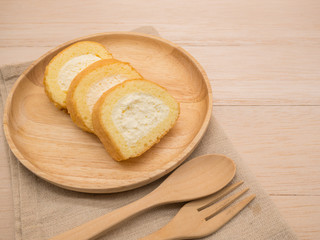 Top view cake roll in wooden plate and wooden fork,spoon on brown fabric and wooden beige table,background with copy space