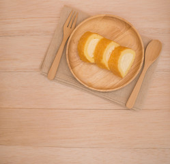 Top view cake roll with wooden fork and spoon on wooden plate and beige wooden table background with copy space 