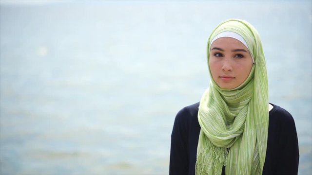 A portrait of a modern Muslim woman who clothed a veil over her head, a lady in a scarf stands near the sea and looks thoughtfully aside