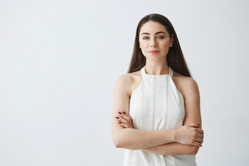Portrait of young beautiful businesswoman looking at camera with crossed arms over white background.