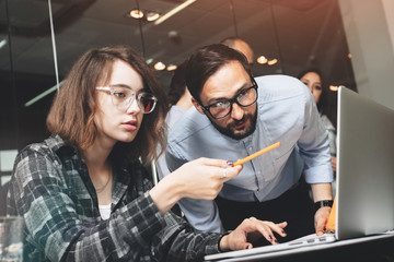 Young and beautiful business woman in glasses with pencil in her hand shows analysis of project to her bearded business partner. Young coworkers working on new startup project in modern office