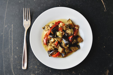 Vegetable stew on white plate on dark textured table