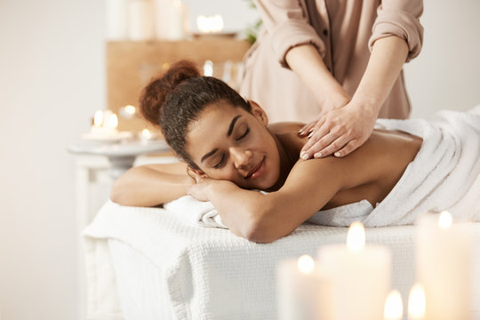 Beautiful African Girl Smiling Enjoying Massage With Closed Eyes In Spa Salon.