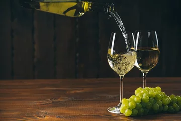 Cercles muraux Vin Pouring white wine into a glass with a bunch of green grapes against wooden background