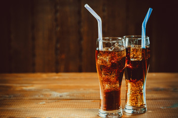 Beautiful cold drink of Cola with ice cubes with a boiler straws in glasses on wooden background with free space