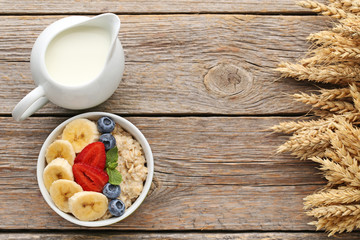 Oatmeal in bowl with berries and milk on wooden table