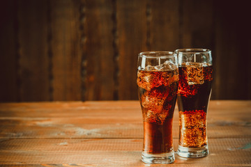 Beautiful cold fizzy cola soda with cubes ice in glasses goblet on old wooden background with free space