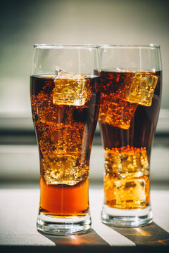 Beautiful cold drink of Cola with ice cubes in a glass on a grey window background with free space