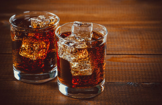 Beautiful cold fizzy cola soda with cubes ice in glasses goblet on old wooden background with free space