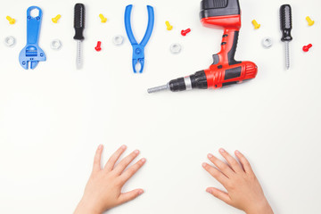 Top view on child's hands with colorful toys tools on the white background.