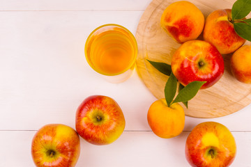 Glass of juice and ripe apples and peaches on a wooden table. Juice and fresh fruits on a light background. Copy Space