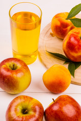 Glass of juice and ripe apples and peaches on a wooden table