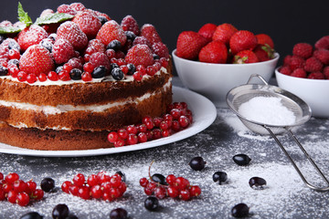 Homemade biscuit cake with berries and powdered sugar on grey wooden table