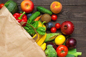 Full paper bag of different fruits and vegetables on rustic wooden background