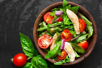 Fresh salad with chicken breast, arugula, basil and tomato over dark stone background